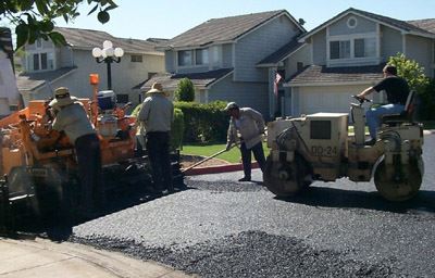 A crew of four work on applying overlay to a road in a residential neighborhood.