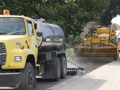 Two trucks work on applying sealcoat.